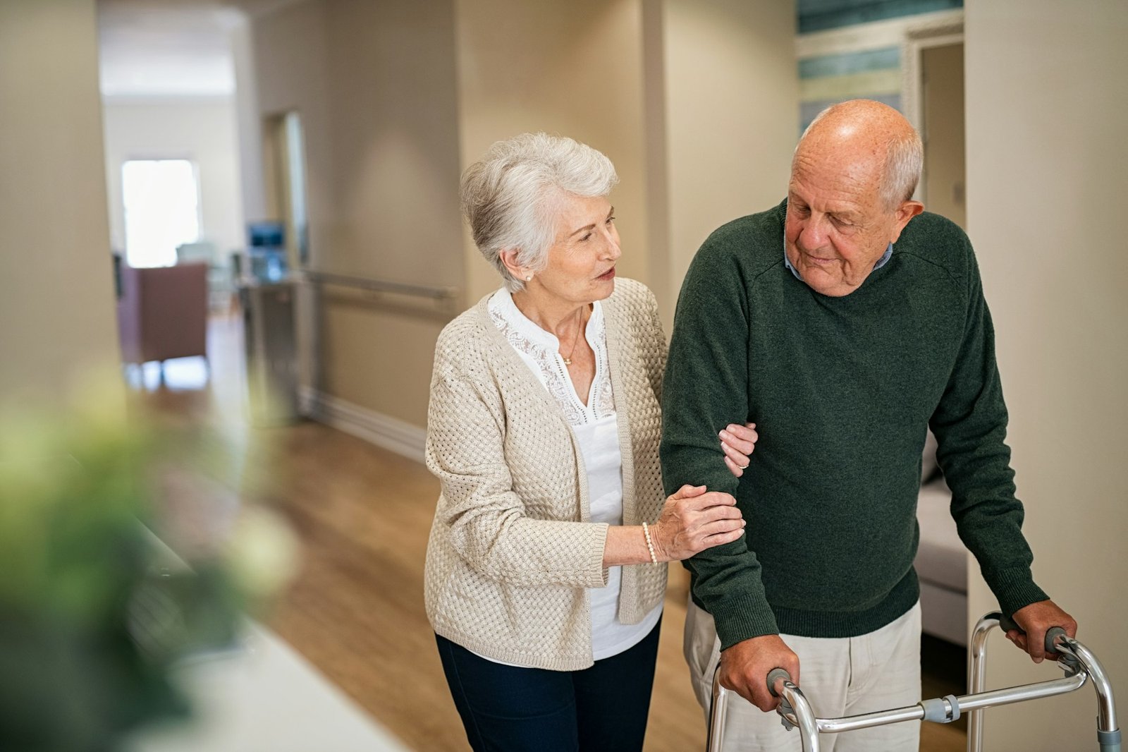 Senior woman helping disabled husband walk at medical clinic