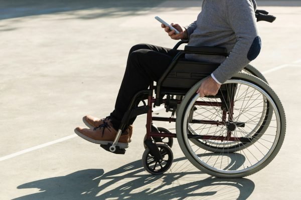 Man in wheelchair using a mobile phone outdoors.